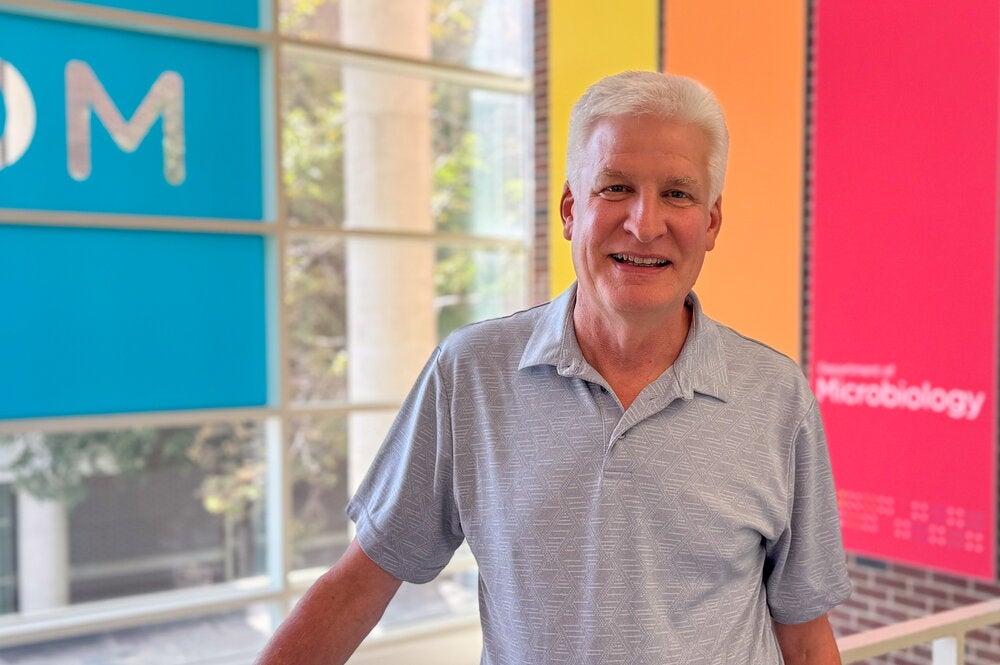 Man in blue polo stands in lab atrium with colorful signs in background